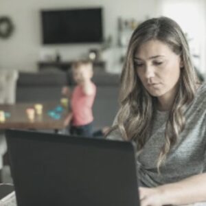 Sad mother on laptop with kids in the background
