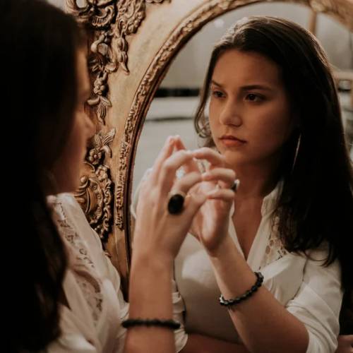 Woman looking and touching mirror with a longing look on face.